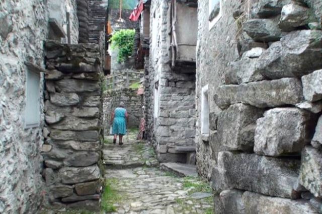 Senhora caminha por uma rua estreita de Corippo, ladeada por construÃ§Ãµes de pedra (Foto: BBC)